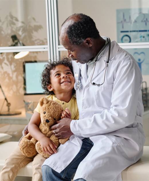 African male doctor giving toy to little patient and talking to him during medical exam at hospital